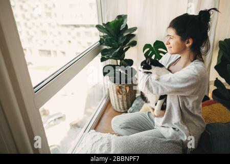 Bleiben Sie zu Hause bleiben Sie sicher. Hipper-Mädchen umarmt süße Katze und sitzt zu Hause während der Quarantäne des Coronavirus zusammen. Isolierung zu Hause, um Virus-Epim zu verhindern Stockfoto