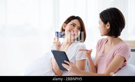 Zwei asiatische Frauen verwenden Tablet für Online-Shopping-Zwecke und zahlen mit Kreditkarte. Stockfoto