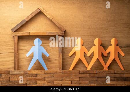 Blaue Papierausschnitte menschliche Figur in einem Holzblock, der nach Hause gebaut wurde, und drei weitere orangefarbene Papierausschnitte außerhalb des Holzhauses auf Holzrückenholz Stockfoto