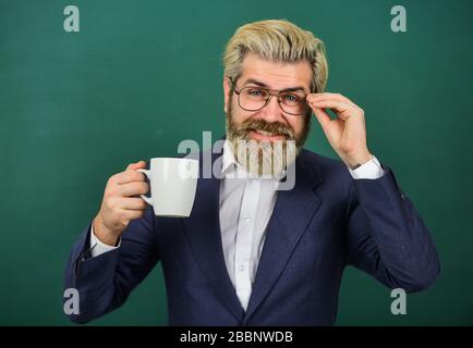 Optimistisches Konzept. Lehrer in der Brille trinken Kaffee Kelkboard Hintergrund. Angenehmer Schluck. Kaffeepause und Entspannung. Mittagszeit für Lehrer. Kaffeesüchtig. Energieaufladung für den ganzen Tag. Koffeindosis. Stockfoto