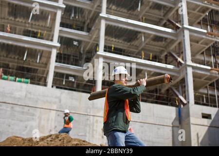 Bauarbeiter tragen einen Hut und tragen ein großes Rohr auf einer Außenbaustelle. Stockfoto