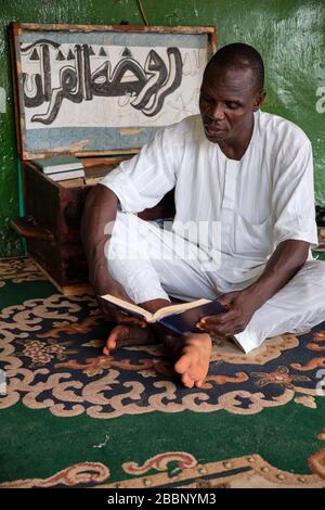 Muslimischer Mann, der auf dem Boden sitzt und den heiligen Koran liest. Stockfoto