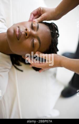 Junge Frau, die eine Kopfmassage mit geschlossenen Augen erhält. Stockfoto