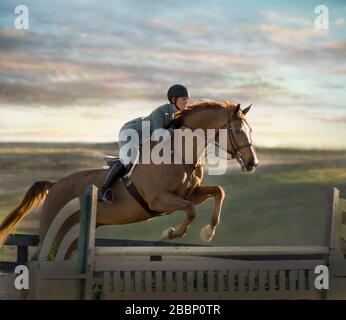 Mädchen im Alter von Teenagern, die auf dem Pferd reiten und beim Springwettbewerb ein Hindernis überwinden. Stockfoto