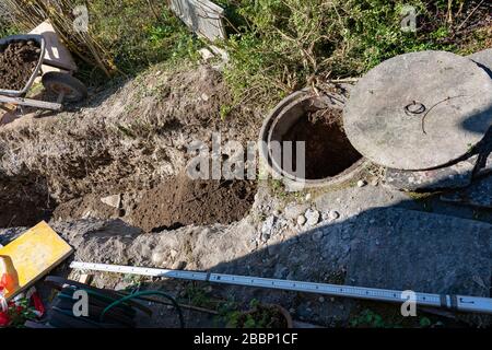 Blick auf die Baustelle des Abwasserschachts. Schubkarre gefüllt mit schwerem Boden, metrisches Maß auf dem Boden. Konzept. Stockfoto