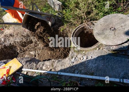 Hochwinkeliger Blick auf Bauarbeiter, die eine Schubkarre Erde abwerfen. Baustelle des Abwasserschachts mit metrischem Maß auf dem Boden. Konzept. Stockfoto