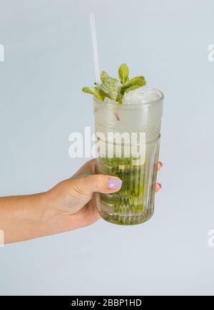 Nahaufnahme der Hand eines Mannes mit einem Glas tropischem Mojito-Cocktail auf orangefarbenem Hintergrund mit Kopierraum. Sommerurlaub Konzept. Stockfoto