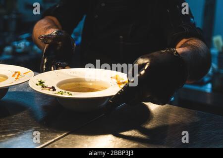 Der Küchenchef im Restaurant bereitet Gerichte zum servieren an der Theke zu. Nahaufnahme von Handschuhen Stockfoto