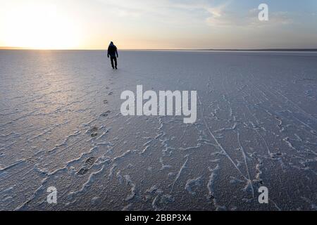 Mann, der auf salzigem Boden läuft, Spuren von Fußspuren in der dramatischen Landschaft am Salzsee Tuzbair, Aktau, Mangystau, Kasachstan, Stockfoto