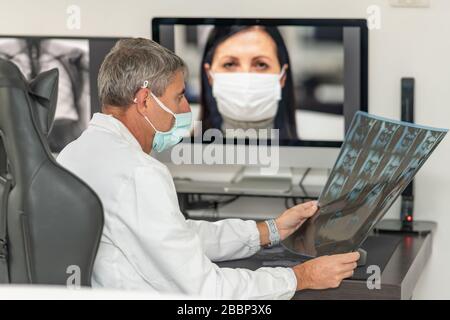 Rückansicht des Arztes, der Videoanruf mit seinem Patienten zu Hause mit Maske macht. Nahaufnahme des Patienten in Videokonferenzen mit Allgemeinmedizinern mit Stockfoto