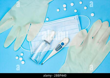 Coronavirus Schutz und Behandlung: Medizinische Maske, Hand Antiseptikum, Handschuhe, Thermometer und Pillen auf blauem Hintergrund. Stockfoto