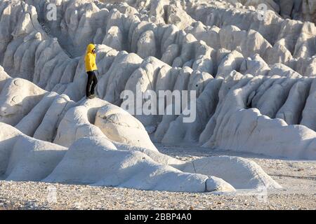 Frau in gelber Jacke auf weißen Felsformationen in der dramatischen Landschaft am Tuzbair Salzsee, Aktau, Mangystau, Kasachstan, Stockfoto