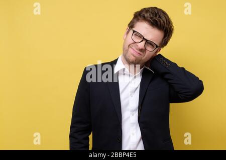Reifer gestresster Geschäftsmann, der seine Hände am schmerzenden Hals hält. Studio auf gelbem Hintergrund aufgenommen. Stockfoto