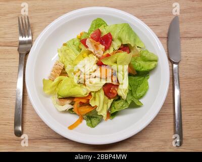 Gemischter grüner Salatsalat, Plattenbesteck, Holztisch, in Scheiben geschnittene Grüns, Gemüsesorten, Tomaten, geröstete Hühnerstücke - leicht, gesund Stockfoto