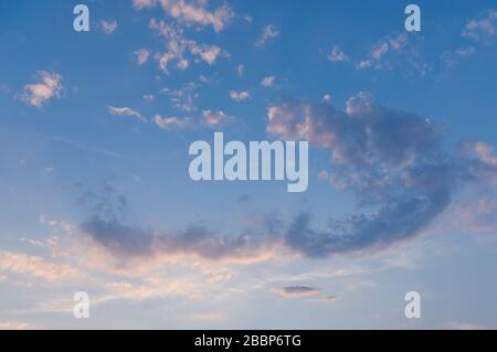 Blauer Himmel mit weißen Wolken in Bogenform mit roter Farbgebung bei Sonnenuntergang bei Sonnenschein am Abend Stockfoto