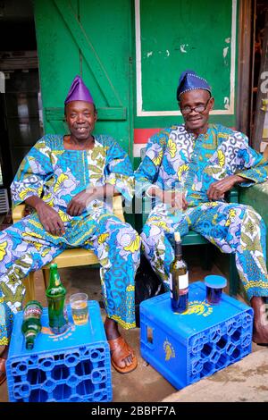 Zwei Männer mit farbenfrohem traditionellen nigerianischen Anzug, die auf einer Terrasse Wein trinken. Stockfoto