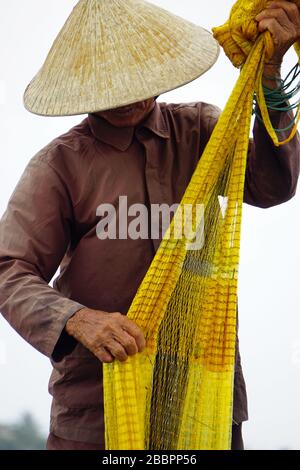 vietnamesischer Fischer auf kleinem Boot angeln mit Fischnetz Stockfoto