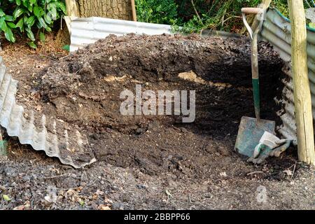 Ein Komposthaufen mit Wellblechseiten, Spaten- und Gartenhandschuhen. Stockfoto