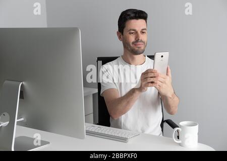 Ein Mann arbeitet von zu Hause aus mit seinem Telefon und Computer. Telearbeit-Konzept Stockfoto