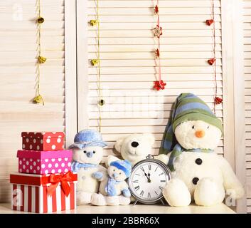 Schneemänner, Teddybären und präsentieren Kisten in der Nähe des Weckers. Celebration und Neujahrsdekor. Weihnachtsdekoration im Festsaal. Spielzeuge auf dem Büro auf Holzwand und Girlanden im Hintergrund Stockfoto