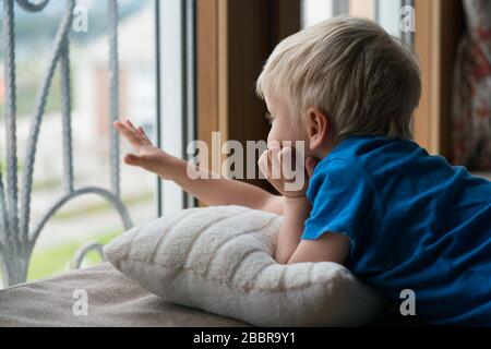 Bleiben Sie zu Hause Quarantäne Coronavirus Pandemieprävention, der vierjährige Junge schaut durch das Fenster, ohne für einen Spaziergang gehen zu können. Stockfoto