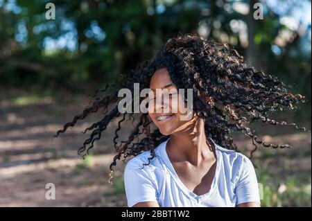 Lächelndes afro-amerikanisches Mädchen, das ihr Haar in der Natur schwingt. Fokus auf Vordergrund. Stockfoto
