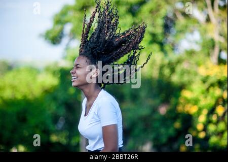 afroamerikanisches Mädchen lächelt und wirft ihr schwarzes Haar hoch. Fokus auf Vordergrund. Stockfoto