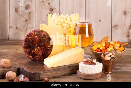Verschiedene Käseklassiker, auf einer alten Holztafel, Nüssen, Snacks und einem Glas Bier. Traditioneller holländischer Käse verschiedener Sorten. Freier Speicherplatz für Text. Stockfoto