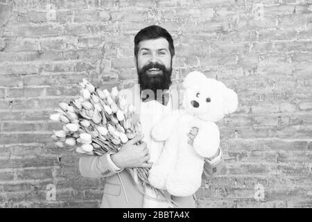 Romantischen Mann. Macho fertig, romantisches Date. Warten auf Darling. Mann gut gepflegt Verschleiß tuxedo Bow Tie halten Blumen Tulpen Bouquet und großen Teddybären Spielzeug. Laden Sie dating. Romantisches Geschenk. Stockfoto