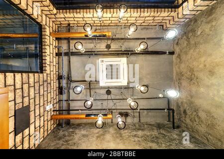 Blick auf die graue Betondecke mit Halogenflecken und edison Lampen im Loft-Büroraum mit Klimaanlage und orangefarbenem Belüftungsrohr Stockfoto