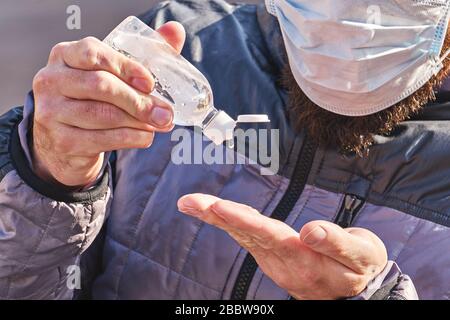 Der Mann, der Maske trägt, verwendet ein antibakterielles Gel auf seinen Händen, das im Park im Freien sitzt. Selbstvorkehrungen während einer Pandemie von Coronavirus. Stockfoto