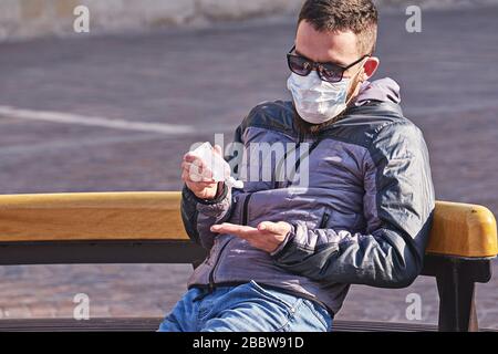 Der Mann, der Maske trägt, verwendet ein antibakterielles Gel auf seinen Händen, das im Park im Freien sitzt. Selbstvorkehrungen während einer Pandemie von Coronavirus. Stockfoto