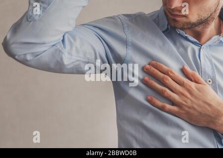 Mann mit Hyperhidrose schwitzt sehr schlecht unter Achselhöhlen in blauem Hemd, auf Grau. Stockfoto
