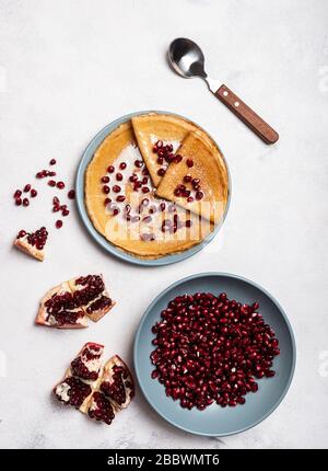 Körner aus geschältem Granatapfel liegen in einer Platte. Pfannkuchen mit Granatapfel und Kondensmilch liegen auf einem Teller. Ansicht von oben. Nahaufnahme. Stockfoto