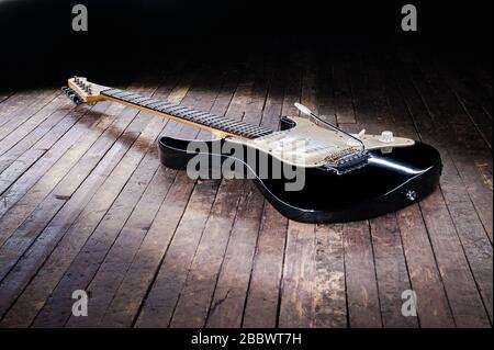 Schwarz-weiße E-Gitarre mit gelbem Signaturstempel liegt auf einer Holzbühne Stockfoto
