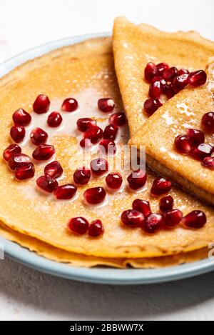 Pfannkuchen mit Granatapfel und Kondensmilch liegen auf einem Teller. Makro. Draufsicht. Stockfoto