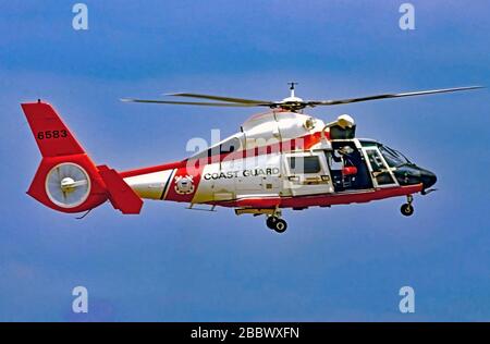 Camp Springs Maryland, USA, 20. Mai 1989 EIN Hubschrauber der United States Coast Guard MH-65 Dauphin Short Range Recovery wechselt in den Hover-Modus, während der Rettungsschwimmer im Rücken sich darauf vorbereitet, den Hebegeschirr im Rahmen einer Demonstration der Fähigkeiten des von Airbus hergestellten Hubschraubers einzusetzen, den die Küstenwache für verschiedene Missionen verwendet, einschließlich Jetzt mit Maschinengewehrversion (MH-65CS) bewaffnet, um das US-Kapitol zu schützen Stockfoto