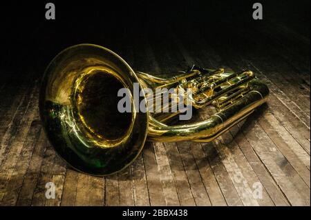 die tuba aus goldenem Messinginstrument liegt im Licht des Scheinwerfers auf einer braunen Holzbühne Stockfoto