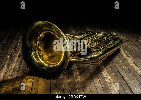 goldenes Blasinstrument Euphonium aus Messing liegt im Licht eines Scheinwerfers auf einer braunen Holzbühne Stockfoto