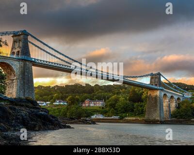 Sonnenaufgang an der Menai Suspension Bridge, die die Insel Anglesey mit dem walisischen Festland verbindet, entworfen von Thomas Telford und eröffnet im Jahr 1826 Stockfoto