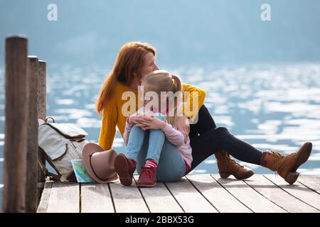 Schöne Mädchen am Pier am Seeufer und Berge im Hintergrund: Mutter und Tochter. Familie im Urlaub Stockfoto