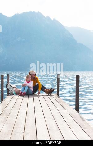 Schöne Mädchen am Pier am Seeufer und Berge im Hintergrund: Mutter und Tochter. Familie im Urlaub Stockfoto
