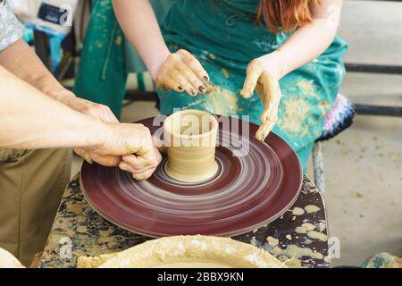 Die Hände eines Meisters und eines Studenten machen einen Krug auf einem Potter-Rad aus gelbem Ton. Selektive Fokussierung auf die Hände Stockfoto
