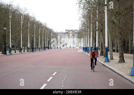 London, Großbritannien. April 2020. Tag Nine of Lockdown in London. Ein Radfahrer fährt entlang einer fast menschenleeren The Mall, mit Buckingham Palace im Hintergrund. Das Land befindet sich aufgrund der COVID-19-Coronavirus-Pandemie in der Sperrstelle. Die Menschen dürfen nicht nach Hause gehen, außer bei minimalem Lebensmitteleinkauf, medizinischer Behandlung, Bewegung - einmal am Tag und wesentlicher Arbeit. COVID-19 Coronavirus Lockdown, London, Großbritannien, am 1. April 2020 Credit: Paul Marriott/Alamy Live News Stockfoto