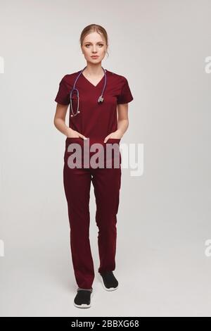 Junge und schöne Frau Tierärztin in Uniform mit Stethoskop, das in voller Länge auf grauem Hintergrund posiert, isoliert Stockfoto