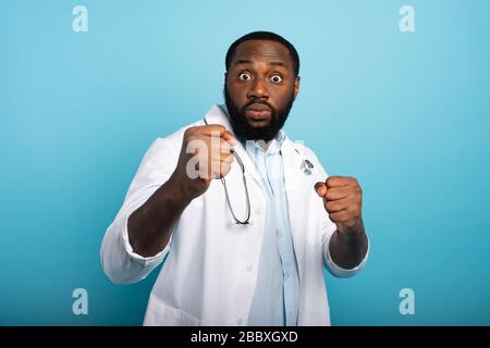 Besorgte Sanitäter werden von einem Kovid-19-Coronavirus angegriffen. Blauer Hintergrund Stockfoto