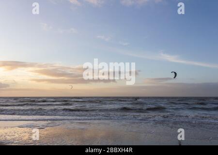 Blick auf den Nordseestrand an einem windigen Wintertag bei Sonnenuntergang, Menschen, Kitesurfen. Noordwijk, Niederlande Stockfoto