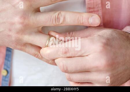 Der Mann entfernt einen goldenen Hochzeitsring aus dem Finger. Begriff des Familienstreits, der Scheidung oder des Verrats. Stockfoto