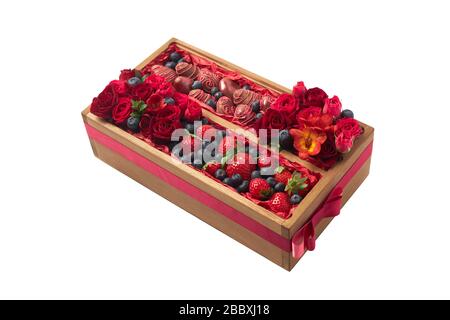 Originalgeschenk in Form einer Holzkiste mit reifen, mit Schokolade überzogenen Erdbeeren, Blaubeeren und roten Blumen auf weißem Grund Stockfoto