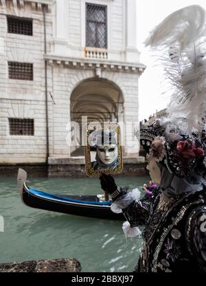 Eine Person in Karnevalsmaske, die sich mit der Brücke der Sichten im Hintergrund an eine Wand eines Gebäudes in Venedig Italien lehnt Stockfoto